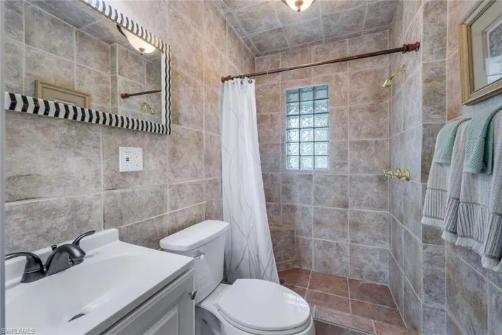 Bathroom with vanity, curtained shower, tile walls, and toilet