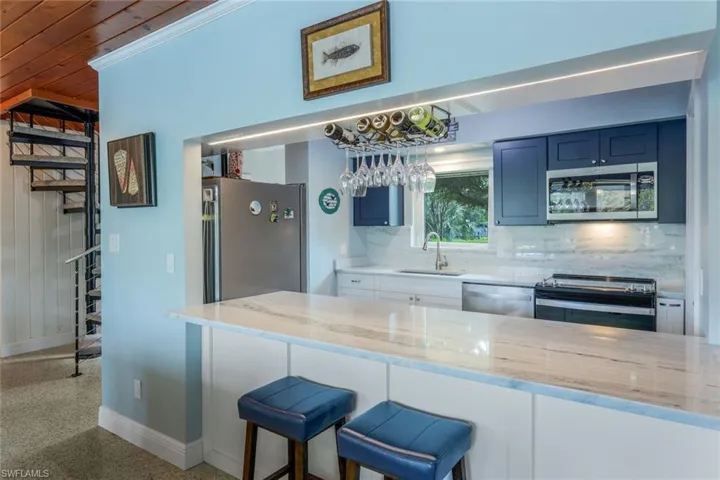 Kitchen with stainless steel appliances, sink, light stone counters, and decorative backsplash