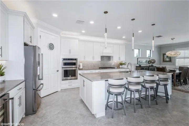 Kitchen with beverage cooler, appliances with stainless steel finishes, an island with sink, light tile patterned flooring, and tasteful backsplash