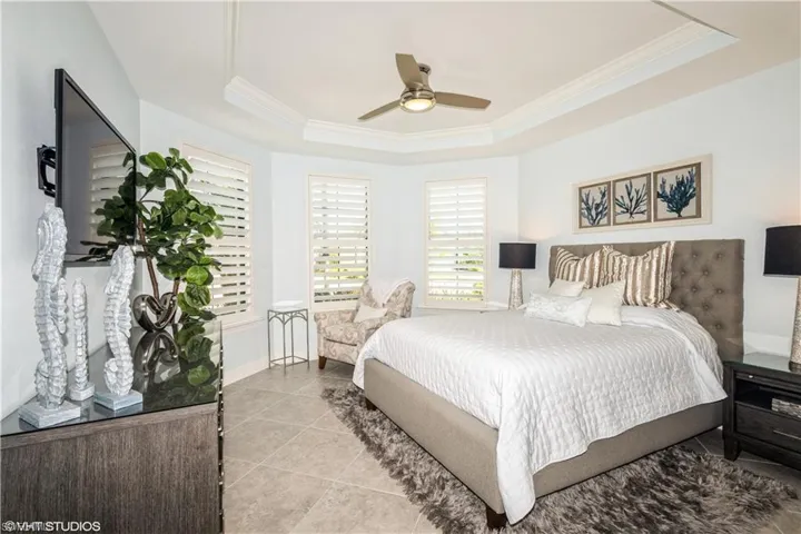 Bedroom with ceiling fan, a raised ceiling, light tile patterned flooring, and ornamental molding