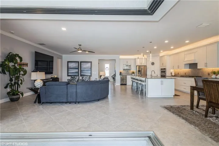 Living room with ceiling fan, light tile patterned flooring, sink, and crown molding