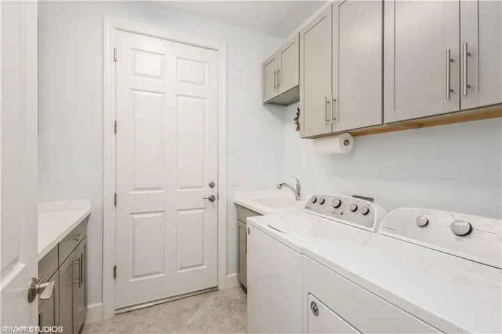 Clothes washing area featuring light tile patterned floors, washer and clothes dryer, cabinets, and sink
