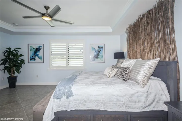 Tiled bedroom featuring a tray ceiling, crown molding, and ceiling fan