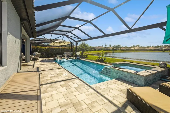 View of swimming pool featuring glass enclosure, an in ground hot tub, a patio area, and a water view