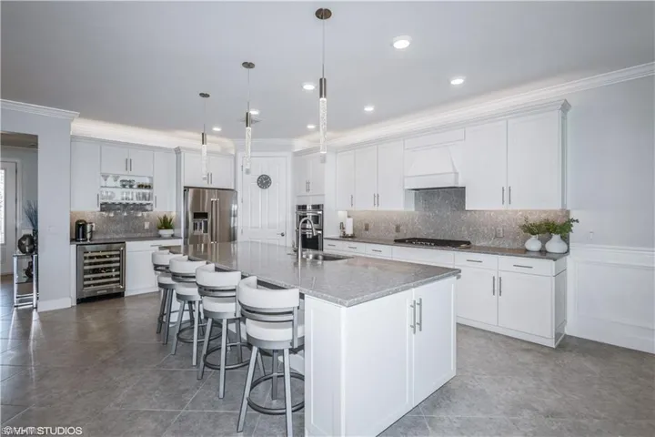 Kitchen featuring stainless steel appliances, beverage cooler, premium range hood, a center island with sink, and sink