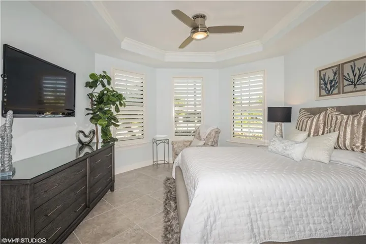 Bedroom featuring ceiling fan, a raised ceiling, light tile patterned floors, and ornamental molding