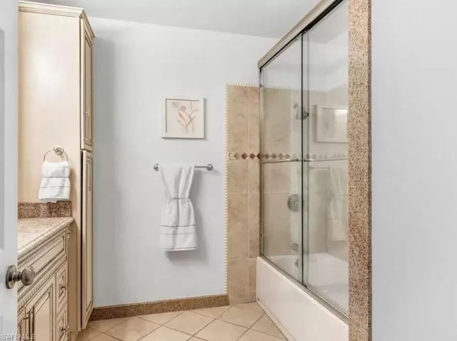 Bathroom featuring vanity, bath / shower combo with glass door, and light tile patterned floors