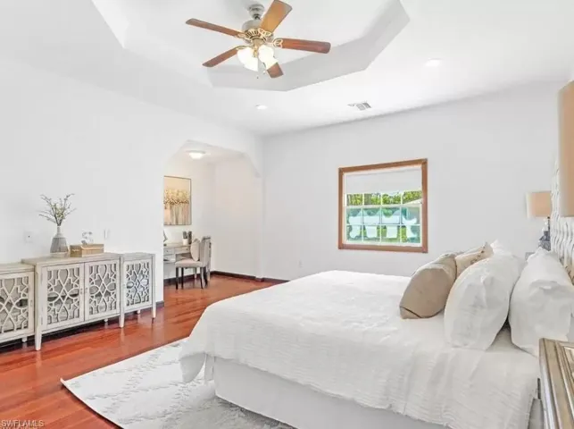 Bedroom with a raised ceiling, arched walkways, a ceiling fan, wood finished floors, and recessed lighting