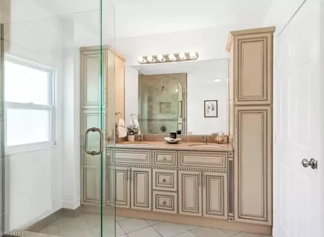Full bath featuring double vanity, light tile patterned floors, and a stall shower