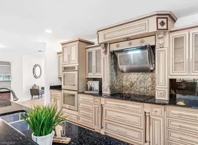 Kitchen featuring cream cabinets, glass insert cabinets, stainless steel double oven, dark stone counters, and recessed lighting