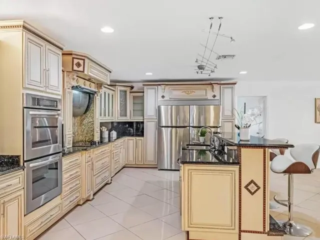 Kitchen with cream cabinetry, a breakfast bar, dark stone counters, glass insert cabinets, and recessed lighting