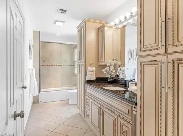 Bathroom with bath / shower combo with glass door, light tile patterned floors, vanity, and a closet