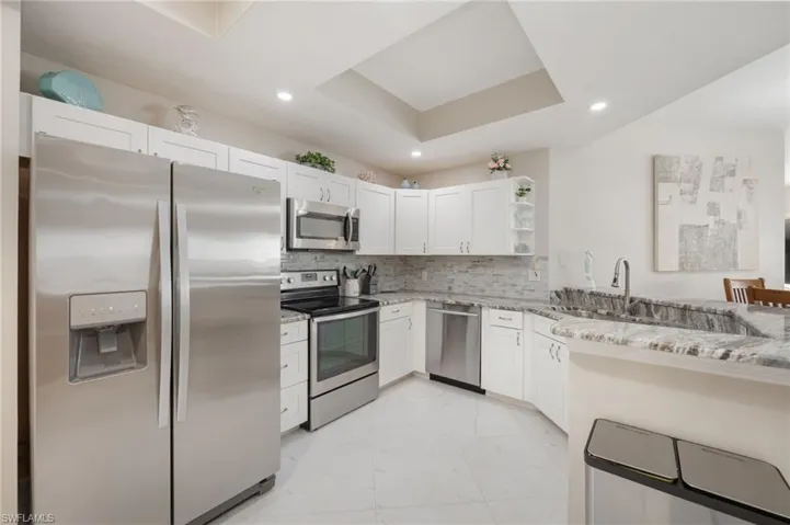 Kitchen with stainless steel appliances, open shelves, a tray ceiling, light stone counters, and backsplash