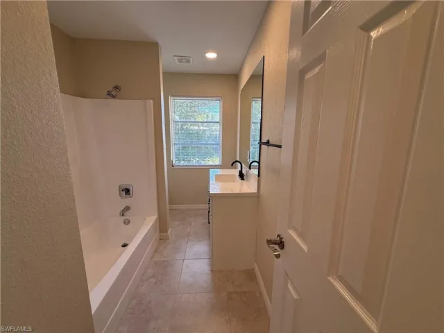 Full bath with vanity, a textured wall, washtub / shower combination, and light tile patterned floors
