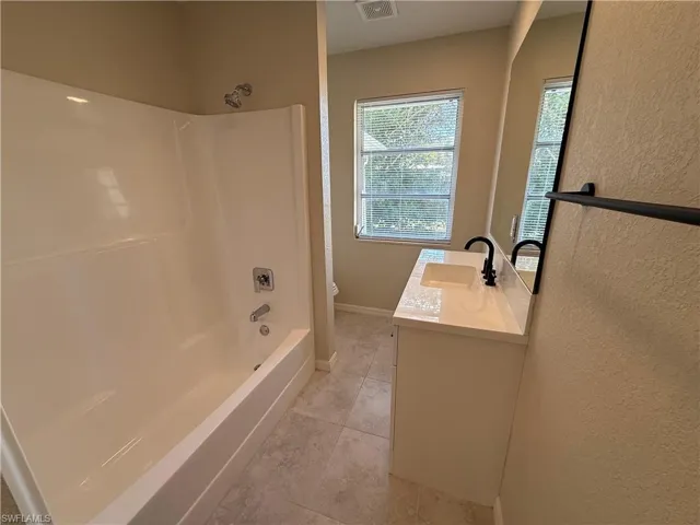 Bathroom with vanity, washtub / shower combination, light tile patterned floors, and a textured wall