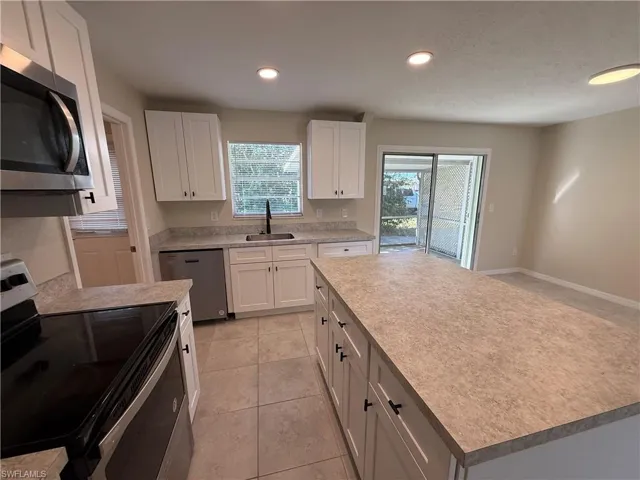 Kitchen with stainless steel appliances, light countertops, white cabinetry, a kitchen island, and light tile patterned floors