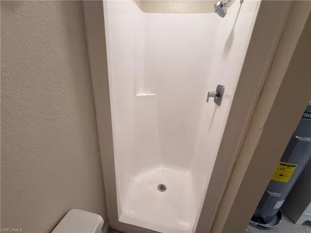 Bathroom with a textured wall, water heater, and a stall shower