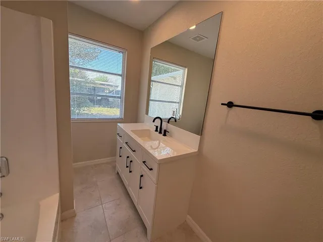 Full bath with vanity, a textured wall, bathtub / shower combination, and light tile patterned floors