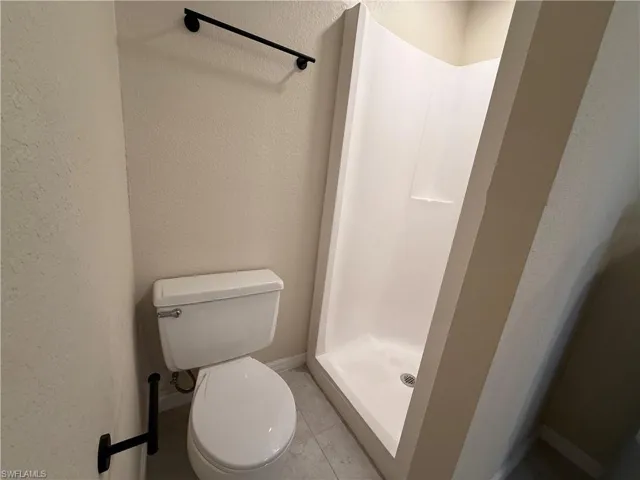 Bathroom featuring a textured wall, a stall shower, and light tile patterned flooring