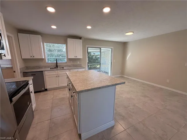 Kitchen featuring stainless steel appliances, light countertops, white cabinets, a kitchen island, and recessed lighting
