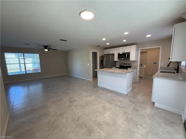 Kitchen featuring white cabinets, stainless steel appliances, open floor plan, a ceiling fan, and light stone countertops