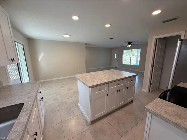 Kitchen featuring open floor plan, white cabinetry, light countertops, freestanding refrigerator, and a kitchen island