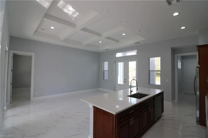 Kitchen featuring sink, stainless steel appliances, coffered ceiling, an island with sink, and beamed ceiling