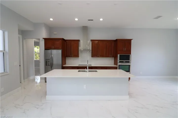 Kitchen with tasteful backsplash, an island with sink, appliances with stainless steel finishes, and wall chimney exhaust hood