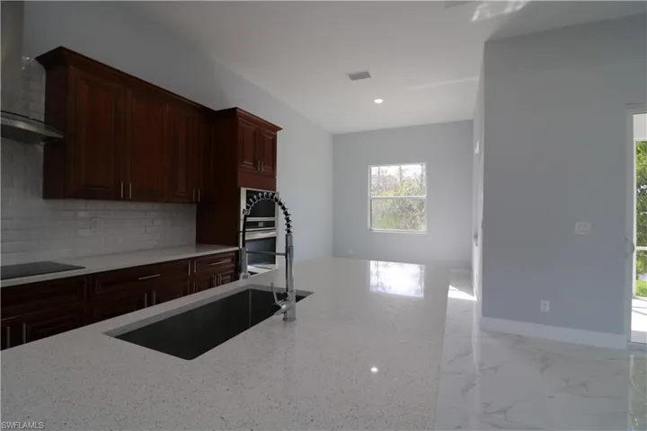 Kitchen featuring wall chimney exhaust hood, sink, tasteful backsplash, black electric cooktop, and light stone countertops