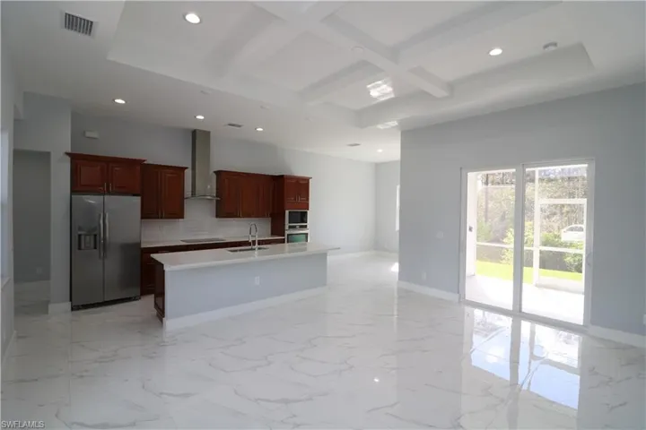 Kitchen with tasteful backsplash, stainless steel fridge, coffered ceiling, a kitchen island with sink, and wall chimney range hood