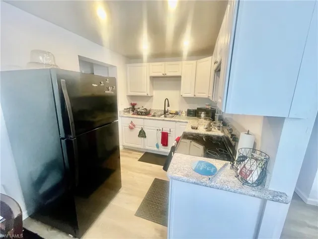 Kitchen with freestanding refrigerator, white cabinetry, light stone counters, and light wood-style flooring