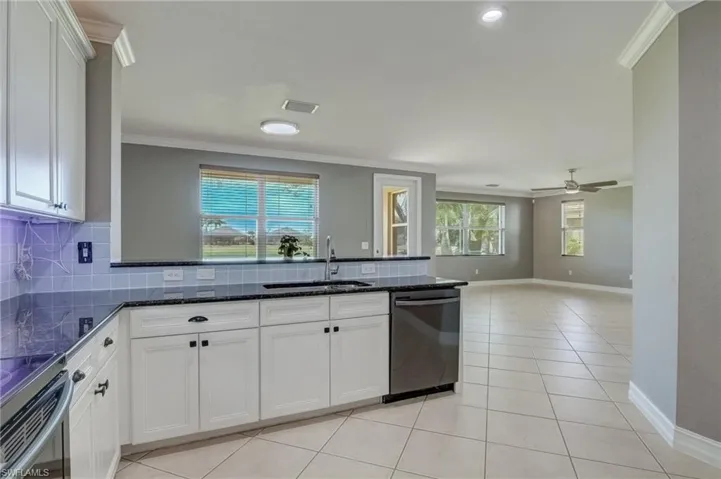 Kitchen featuring sink, white cabinetry, dark stone countertops, ornamental molding, and stainless steel dishwasher