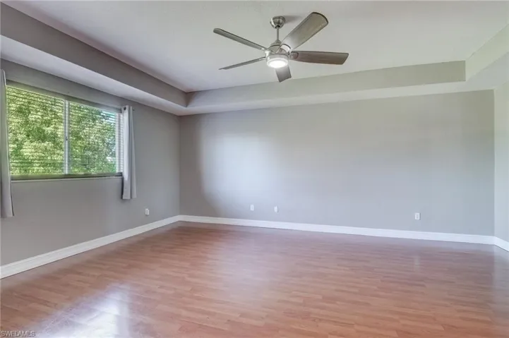 Master bedroom with ceiling fan, a raised ceiling, and light wood-type flooring
