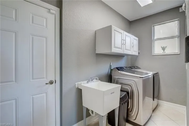 Clothes washing area with cabinets, separate washer and dryer, sink, and light tile patterned floors