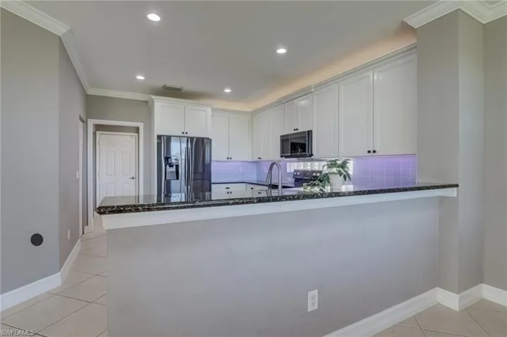 Kitchen featuring appliances with stainless steel finishes, white cabinetry, ornamental molding, light tile patterned floors, and kitchen peninsula
