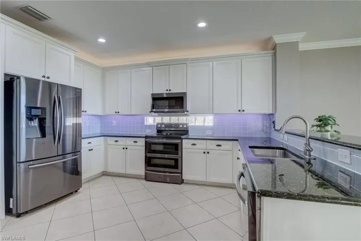 Kitchen with white cabinetry, stainless steel appliances, sink, and dark stone counters