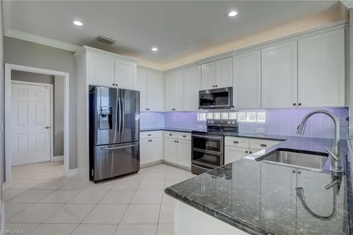 Kitchen with light tile patterned flooring, sink, dark stone countertops, stainless steel appliances, and white cabinets