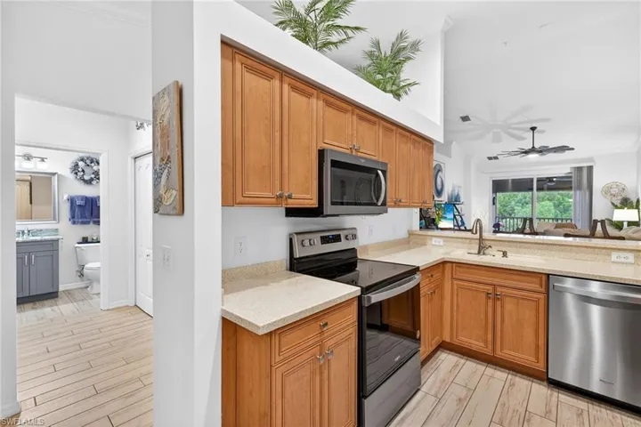 Kitchen with appliances with stainless steel finishes, brown cabinets, light stone countertops, ceiling fan, and wood tiled floors