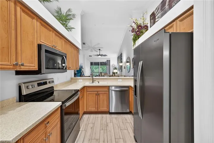 Kitchen with brown cabinetry, appliances with stainless steel finishes, light stone countertops, a ceiling fan, and wood tiled floors