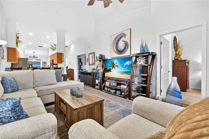 Living room with ceiling fan, wood finished floors, ornamental molding, and a high ceiling