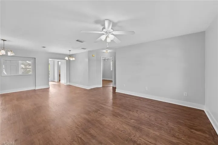 Unfurnished living room featuring ceiling fan with notable chandelier and dark wood-type flooring