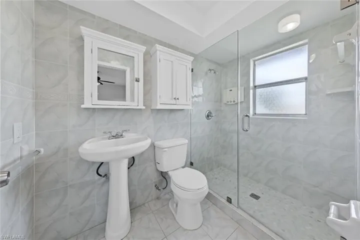 Bathroom featuring an enclosed shower, tile walls, and toilet
