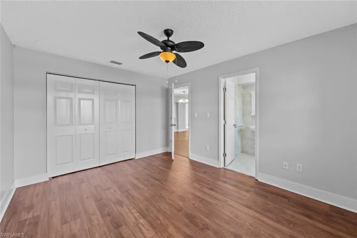 Unfurnished bedroom with ceiling fan, ensuite bathroom, hardwood / wood-style floors, a textured ceiling, and a closet