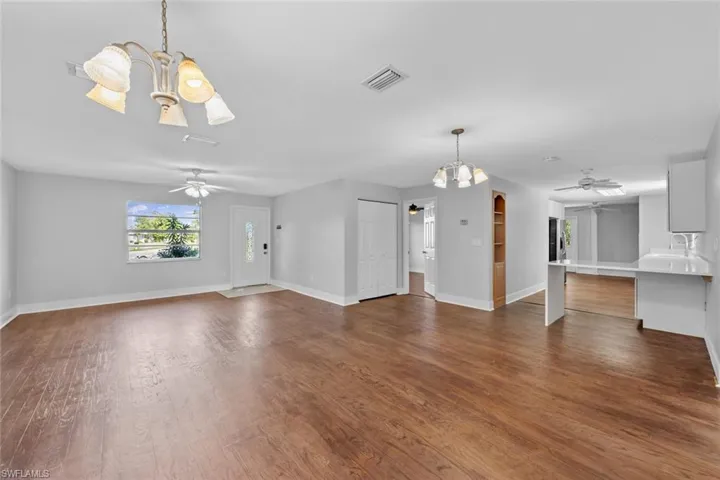 Unfurnished living room featuring sink, dark wood-type flooring, and ceiling fan with notable chandelier