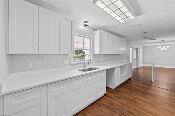 Kitchen featuring ceiling fan with notable chandelier, dark hardwood / wood-style flooring, white cabinetry, and sink