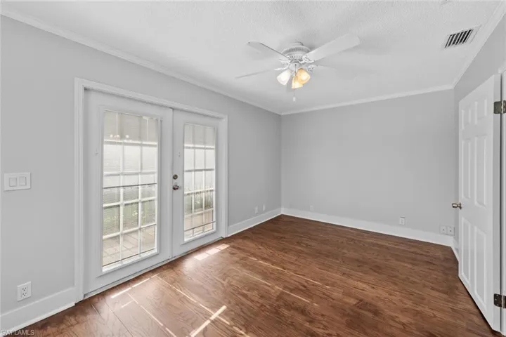 Empty room featuring french doors, ornamental molding, a textured ceiling, ceiling fan, and dark wood-type flooring