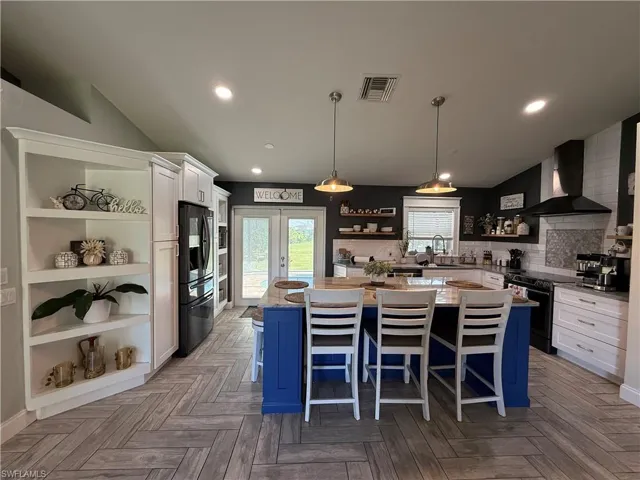 Kitchen featuring open shelves, blue cabinetry, white cabinets, wall chimney exhaust hood, and recessed lighting