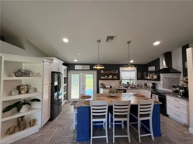 Kitchen with open shelves, blue cabinets, white cabinets, pendant lighting, and wall chimney exhaust hood