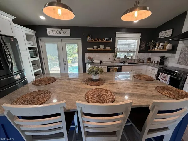 Kitchen with french doors, a breakfast bar, open shelves, black appliances, and light stone counters