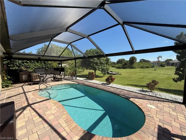 Outdoor pool featuring glass enclosure, an outdoor kitchen, a lawn, a patio, and a sunroom